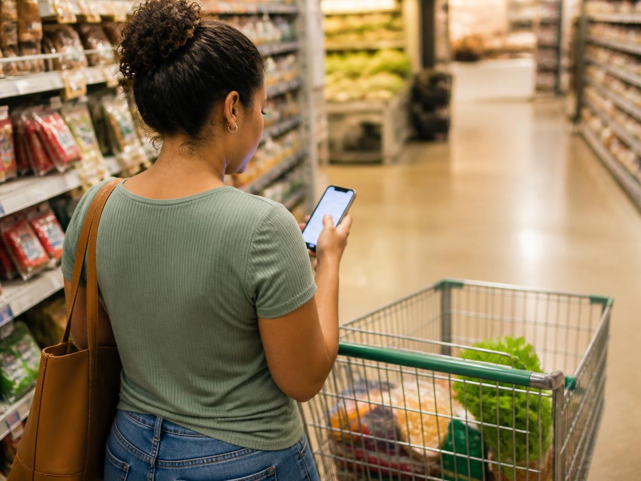 Cliente conferindo o celular enquanto faz compras no supermercado
